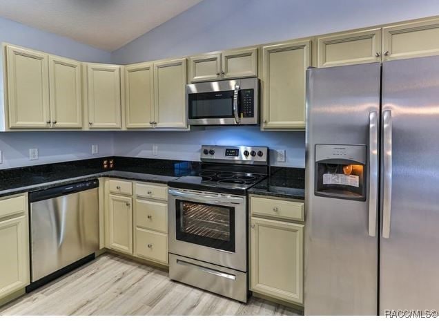 kitchen featuring cream cabinets, dark stone counters, lofted ceiling, and appliances with stainless steel finishes