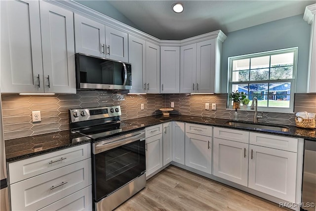 kitchen with decorative backsplash, dark stone countertops, appliances with stainless steel finishes, light wood-style floors, and a sink