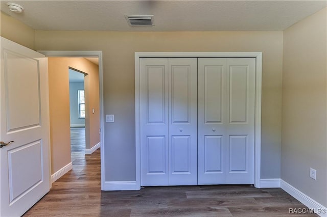 unfurnished bedroom with visible vents, baseboards, a closet, and wood finished floors