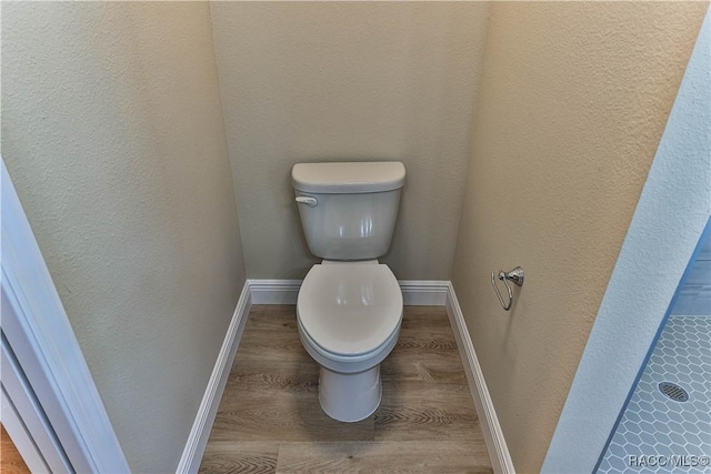 bathroom with a textured wall, toilet, baseboards, and wood finished floors