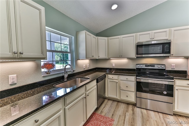 kitchen featuring lofted ceiling, sink, dark stone countertops, light hardwood / wood-style floors, and stainless steel appliances