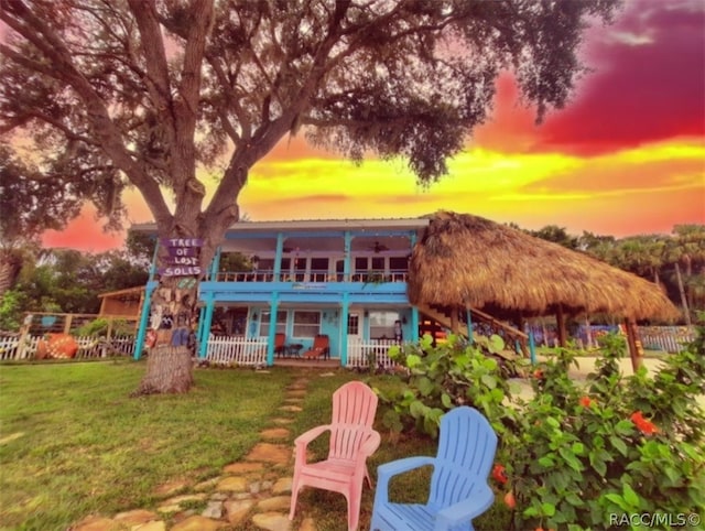 back house at dusk featuring a balcony and a lawn