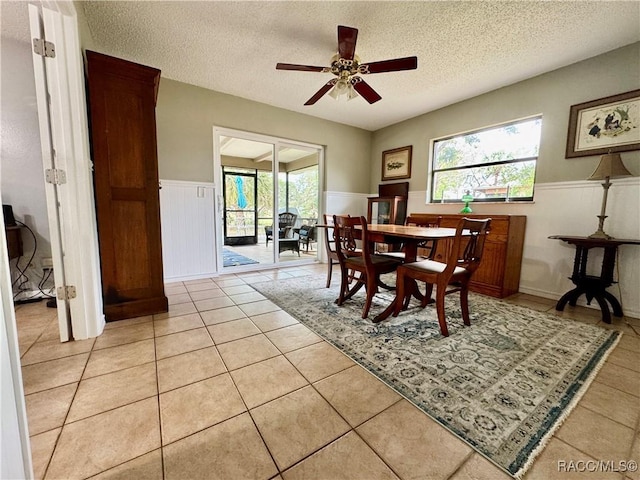 dining space featuring light tile patterned floors, wainscoting, a textured ceiling, and ceiling fan