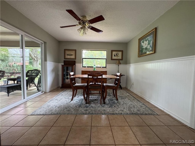 tiled dining area featuring a wainscoted wall, a textured ceiling, and ceiling fan