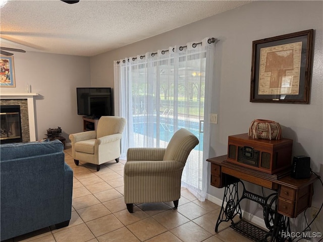 living room with light tile patterned flooring, a glass covered fireplace, a textured ceiling, and a ceiling fan