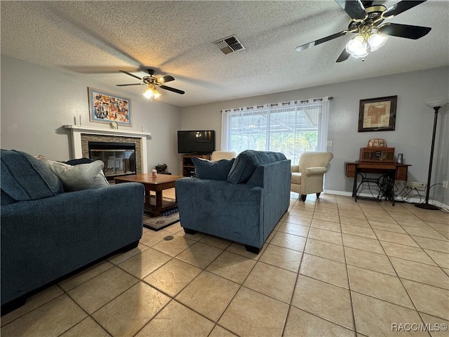 living area with visible vents, ceiling fan, light tile patterned floors, a glass covered fireplace, and a textured ceiling