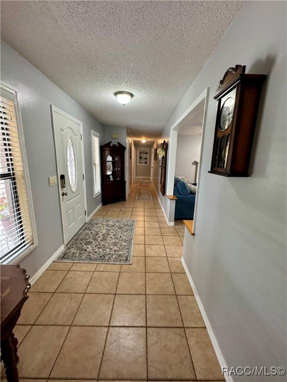 entryway featuring light tile patterned flooring, a textured ceiling, baseboards, and a wealth of natural light