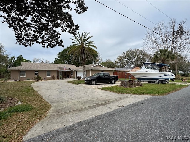 single story home with stucco siding, a front lawn, an attached garage, and driveway