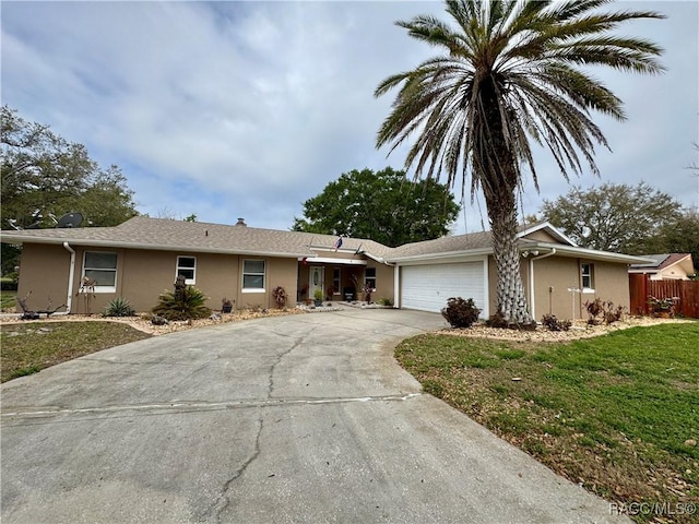 ranch-style house featuring fence, driveway, stucco siding, a front lawn, and a garage