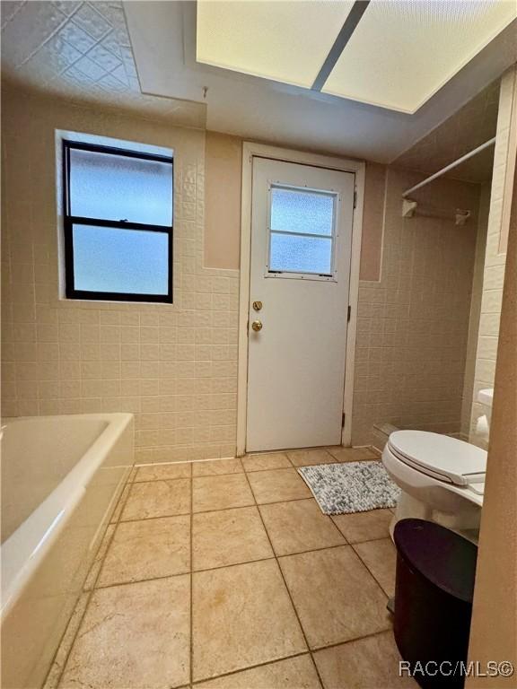 bathroom with a bath, tile patterned flooring, a shower, tile walls, and toilet