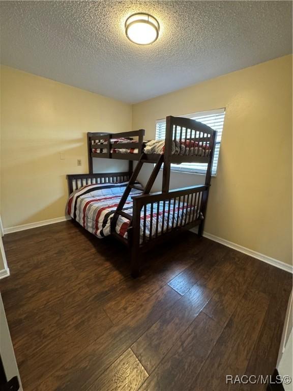 bedroom with a textured ceiling, baseboards, and wood-type flooring