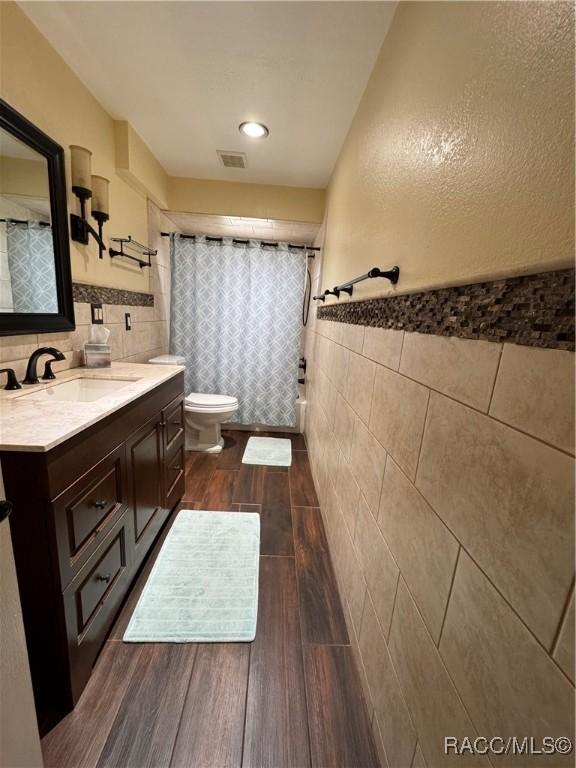 full bathroom featuring visible vents, toilet, tile walls, and wood finished floors