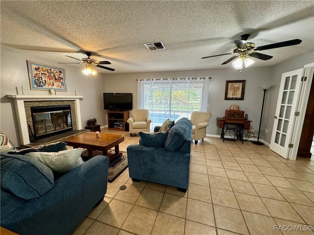 living room with a glass covered fireplace, light tile patterned floors, visible vents, and a textured ceiling