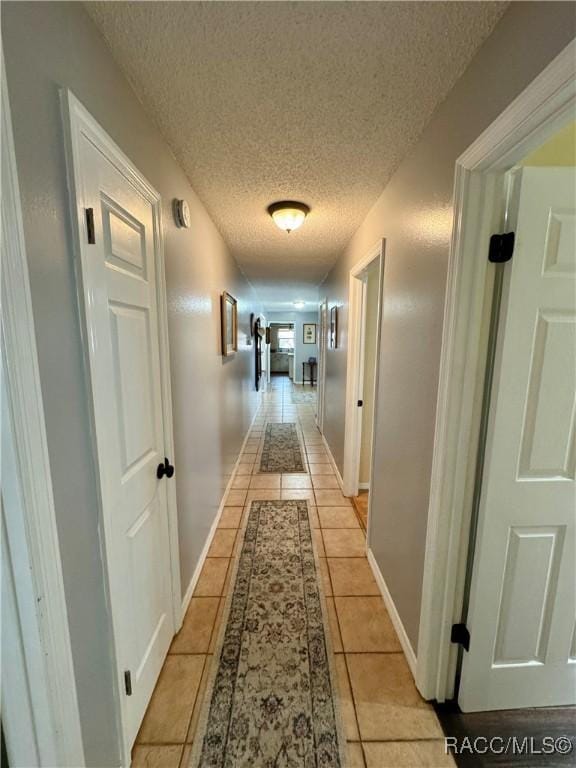 hallway with baseboards, a textured ceiling, and light tile patterned flooring