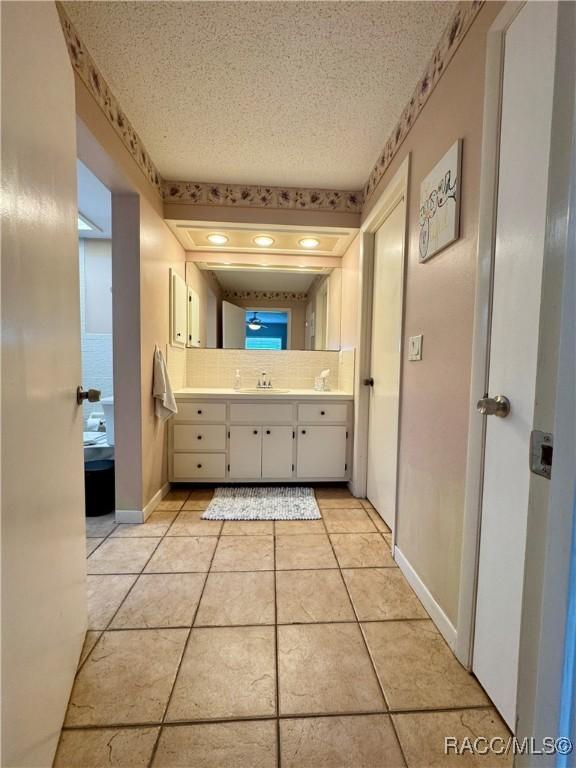 bathroom with baseboards, vanity, decorative backsplash, tile patterned floors, and a textured ceiling