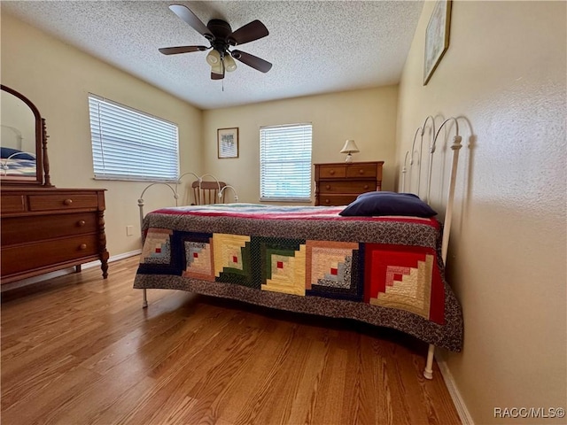 bedroom featuring ceiling fan, a textured ceiling, baseboards, and wood finished floors