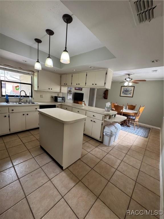 kitchen with visible vents, a sink, decorative light fixtures, a center island, and light countertops