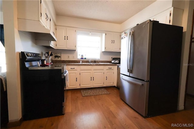 kitchen with electric range oven, sink, light hardwood / wood-style flooring, white cabinets, and stainless steel fridge