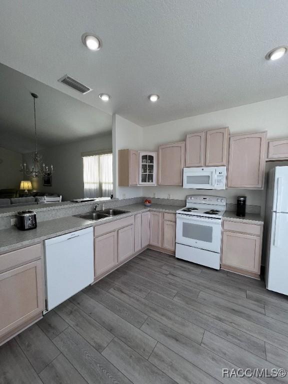 kitchen with sink, decorative light fixtures, white appliances, light brown cabinetry, and a notable chandelier