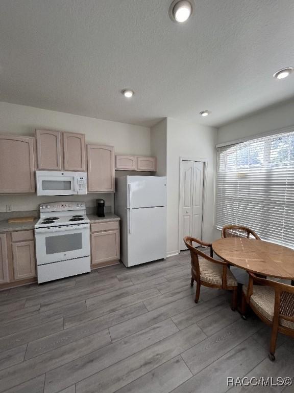 kitchen featuring white appliances, light brown cabinetry, light wood-type flooring, and a textured ceiling