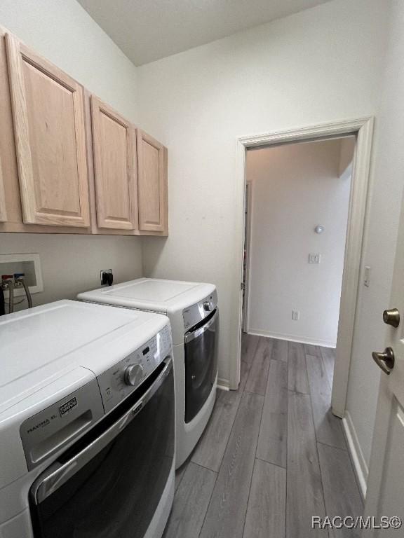 washroom with washer and dryer, cabinets, and light wood-type flooring