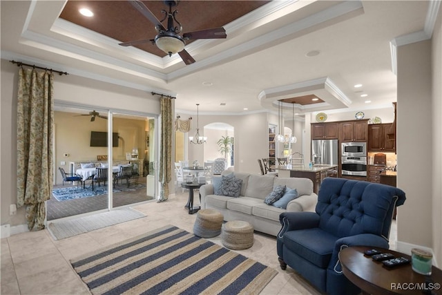 tiled living room with ceiling fan with notable chandelier, a raised ceiling, and ornamental molding