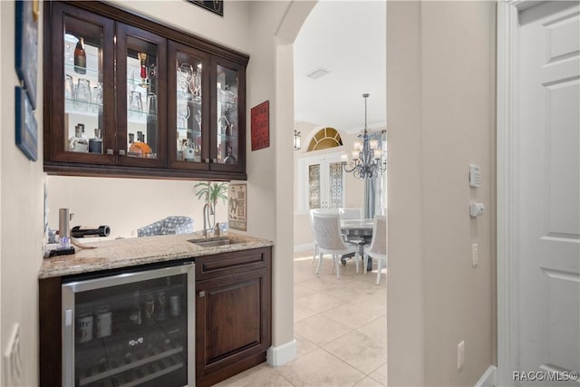 bar featuring dark brown cabinets, light tile patterned flooring, light stone counters, and wine cooler