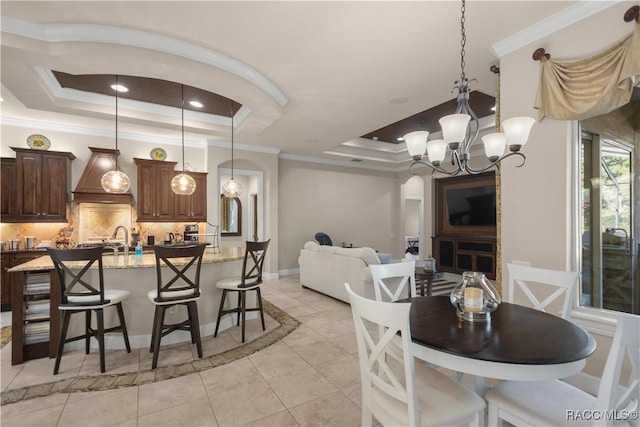 tiled dining area with a tray ceiling, crown molding, sink, and a notable chandelier