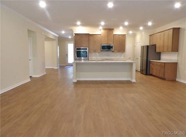 kitchen featuring refrigerator, backsplash, ornamental molding, light hardwood / wood-style floors, and an island with sink