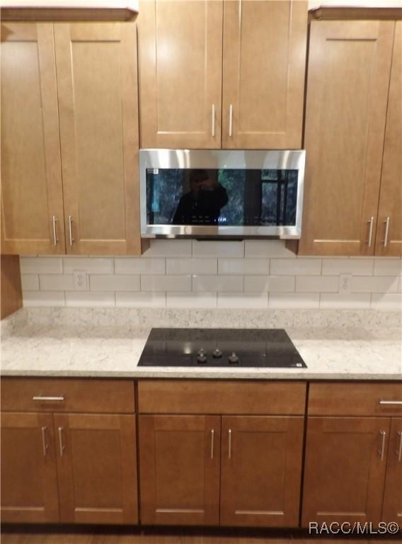 kitchen featuring light stone countertops, black electric stovetop, and backsplash