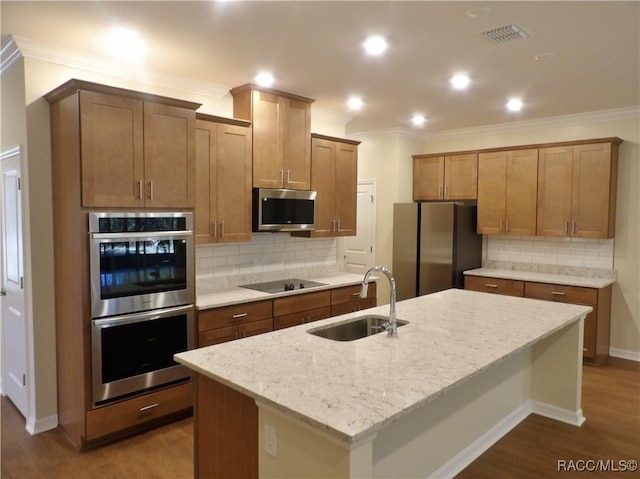 kitchen with sink, appliances with stainless steel finishes, hardwood / wood-style floors, light stone counters, and an island with sink