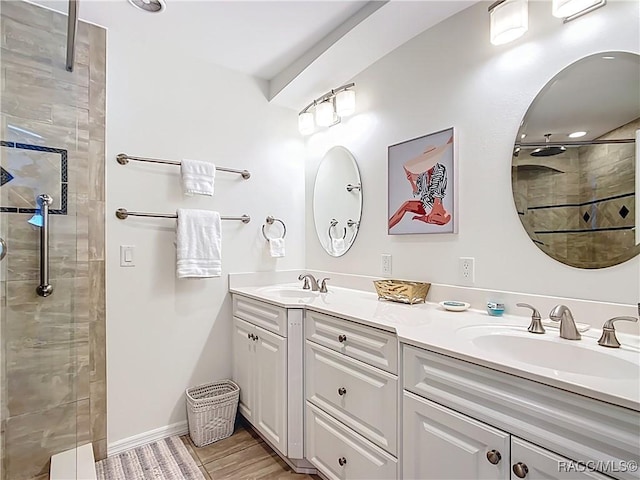 bathroom with double vanity, tiled shower, baseboards, and a sink