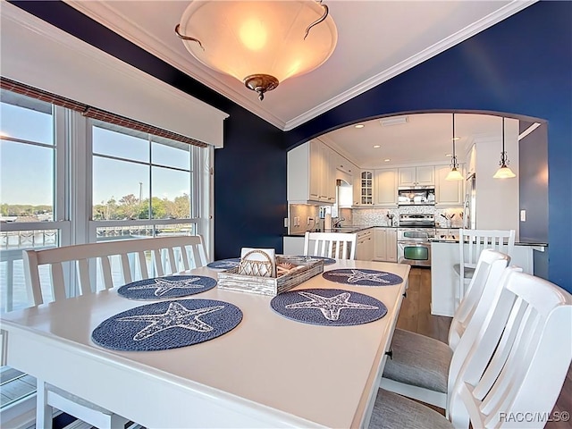 dining space featuring arched walkways, crown molding, and vaulted ceiling