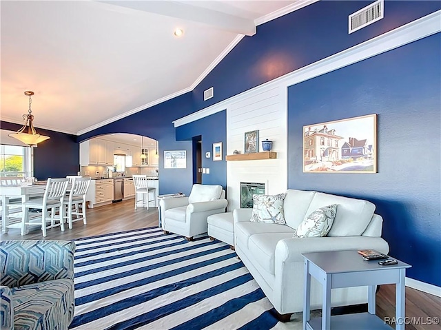 living room featuring lofted ceiling, crown molding, arched walkways, and visible vents