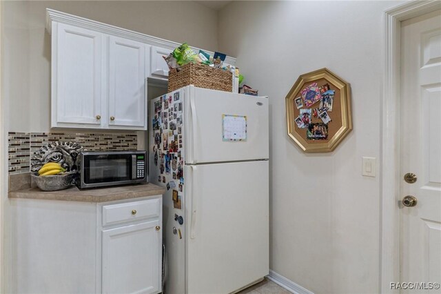 kitchen with freestanding refrigerator, stainless steel microwave, backsplash, white cabinetry, and light countertops