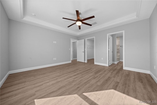 unfurnished bedroom featuring ceiling fan, a spacious closet, a raised ceiling, and light wood-type flooring