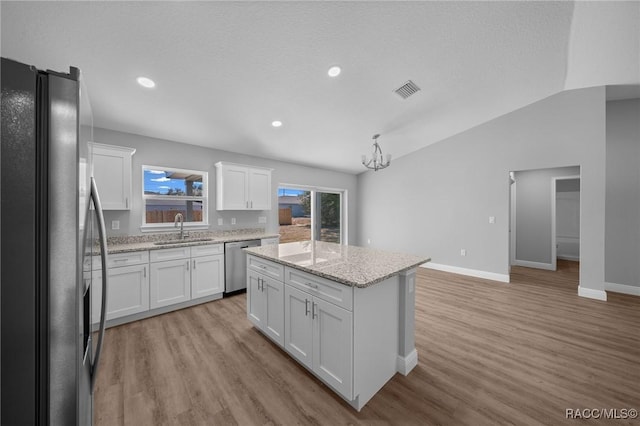 kitchen with sink, appliances with stainless steel finishes, white cabinetry, a center island, and vaulted ceiling