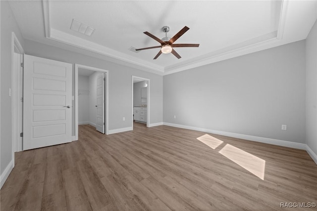 unfurnished bedroom with ensuite bathroom, a spacious closet, a tray ceiling, ceiling fan, and light hardwood / wood-style floors