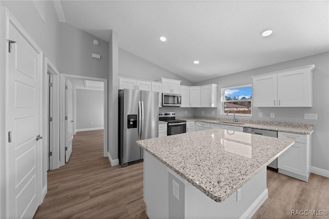 kitchen with appliances with stainless steel finishes, sink, white cabinets, a center island, and light stone countertops