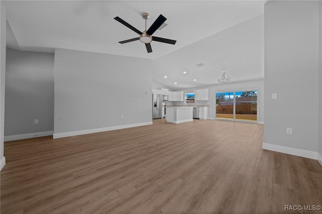 unfurnished living room with vaulted ceiling, ceiling fan with notable chandelier, and light hardwood / wood-style floors