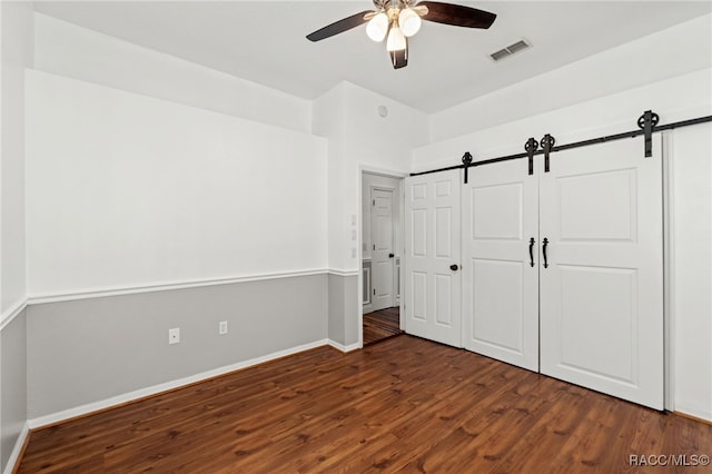 unfurnished bedroom featuring ceiling fan, a closet, dark hardwood / wood-style flooring, and a barn door