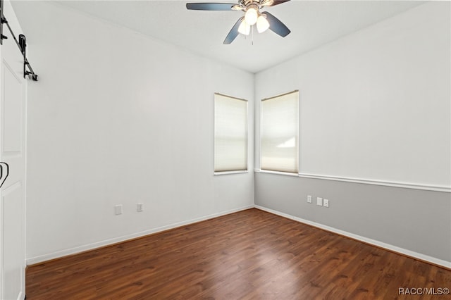 spare room featuring ceiling fan, a barn door, and dark hardwood / wood-style flooring