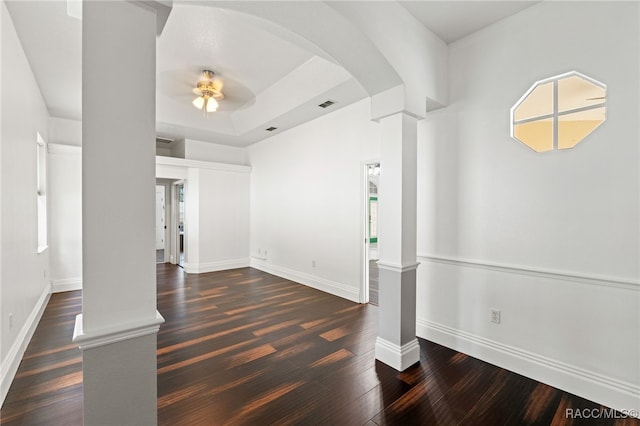 unfurnished living room featuring decorative columns, dark wood-type flooring, a tray ceiling, and ceiling fan