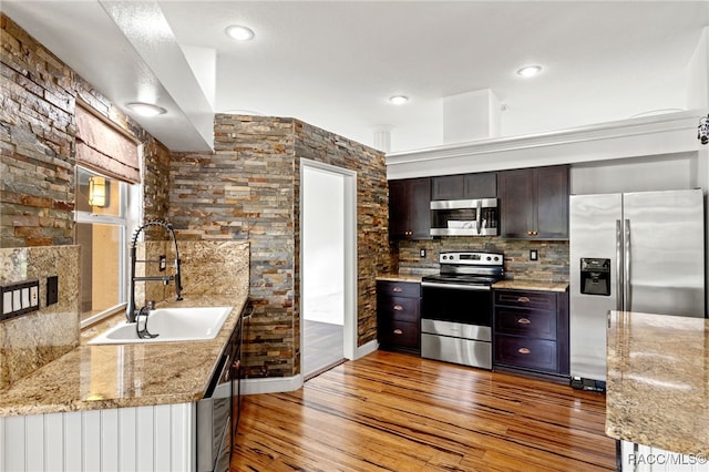 kitchen with kitchen peninsula, sink, dark brown cabinetry, light stone countertops, and stainless steel appliances