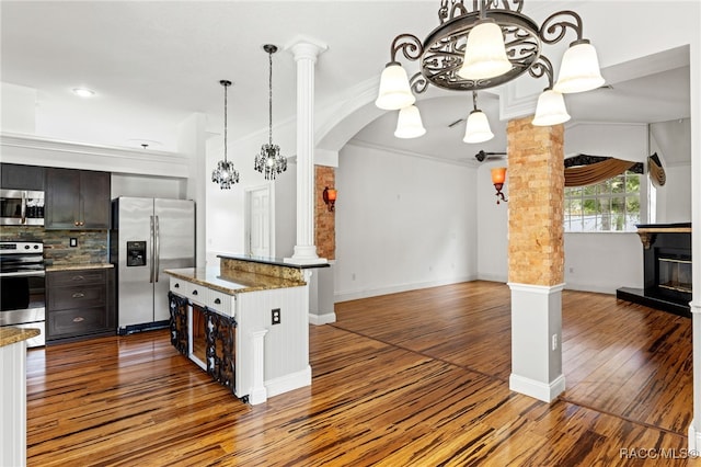 kitchen featuring decorative columns, appliances with stainless steel finishes, crown molding, dark brown cabinetry, and a center island