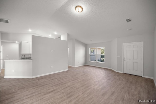 unfurnished living room with a textured ceiling, vaulted ceiling, light hardwood / wood-style floors, and sink