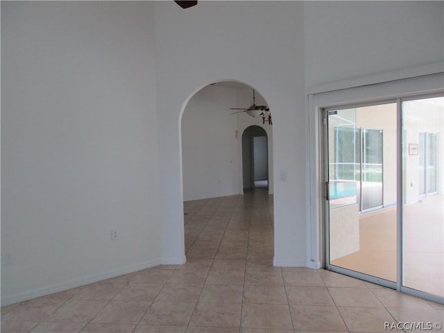 empty room featuring ceiling fan, light tile patterned floors, and a high ceiling