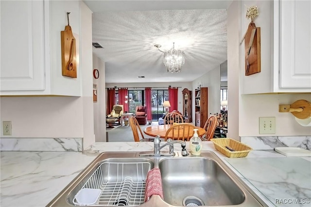 kitchen featuring sink, an inviting chandelier, a textured ceiling, light stone countertops, and white cabinets