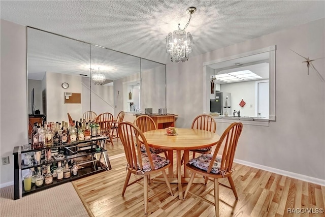 dining area with an inviting chandelier, light hardwood / wood-style floors, and a textured ceiling