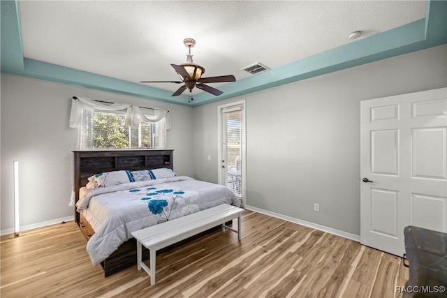 bedroom with light wood finished floors, visible vents, and a tray ceiling